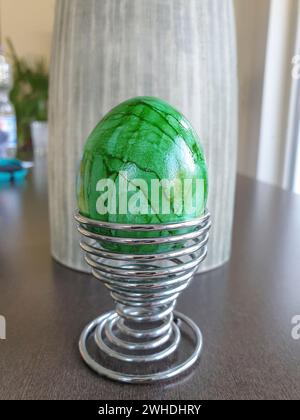 Un uovo verde bollito tinto in una moderna tazza di uovo di Pasqua su un tavolo di legno Foto Stock