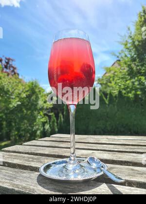 Cocktail analcolico Wild Berries Dreams servito in un bicchiere di vino su una terrazza con giardino verde sullo sfondo Foto Stock