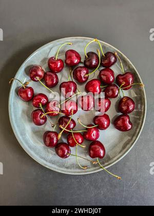 Le ciliegie rosse scure appena raccolte giacciono su un piatto grigio Foto Stock