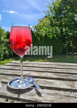 Cocktail analcolico Wild Berries Dreams servito in un bicchiere di vino su una terrazza con giardino verde sullo sfondo Foto Stock