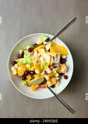 Mele a fette e uva d'arancia di mango servite come Macedonia di frutta in un recipiente con coltello e forchetta Foto Stock