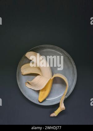 banana gialla sbucciata a metà su un piatto azzurro Foto Stock
