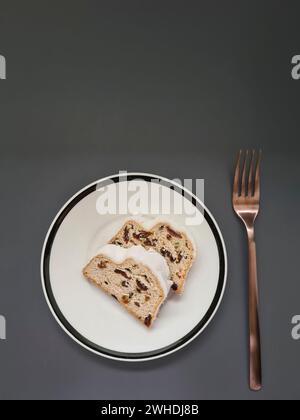 Due fette di torta di Natale con zucchero bianco a velo su un piatto bianco con bordo nero e forchetta color rame Foto Stock