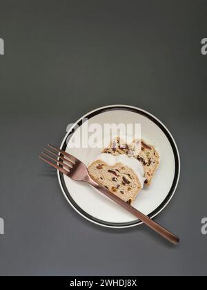 Due fette di torta di Natale con zucchero bianco a velo su un piatto bianco con bordo nero e forchetta color rame Foto Stock