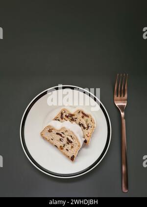 Due fette di torta di Natale con zucchero bianco a velo su un piatto bianco con bordo nero e forchetta color rame Foto Stock