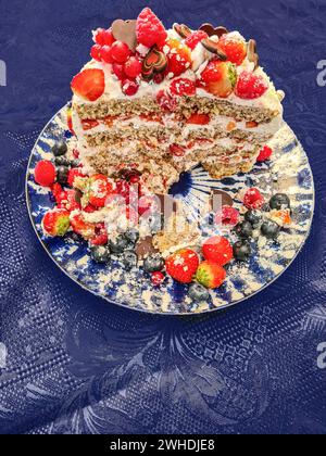 Una torta alla panna natalizia con frutta come fragole, lamponi, ribes e mirtilli mentre la decorazione viene tagliata e mostra la sezione trasversale del c Foto Stock