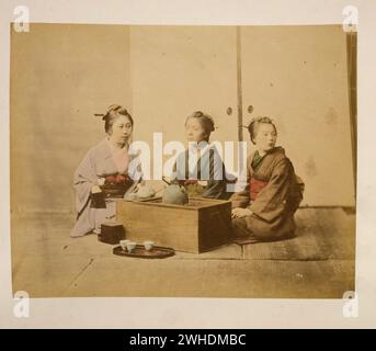 Tre donne che bevono il tè seduto sul pavimento attorno a un tavolo di legno....Giappone colorato a mano con stampe fotografiche ad acquerello intorno agli anni '1870 Foto Stock