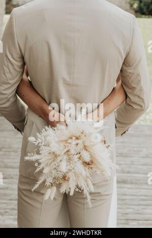 La sposa abbraccia lo sposo con un bouquet di fiori secchi, un anello di matrimonio e di fidanzamento Foto Stock