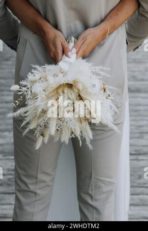 La sposa abbraccia lo sposo con un bouquet di fiori secchi, un anello di matrimonio e di fidanzamento Foto Stock