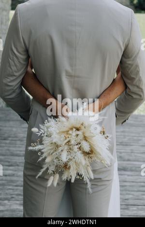 La sposa abbraccia lo sposo con un bouquet di fiori secchi, un anello di matrimonio e di fidanzamento Foto Stock