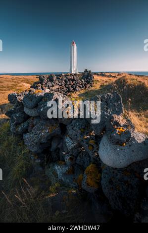 Faro con muro di pietra in primo piano su un prato giallo dorato sulla costa di Arnarstapi sulla penisola di Snæfellsnes nell'Islanda occidentale Foto Stock