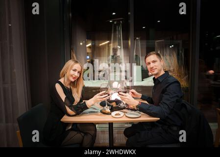 Elegante coppia di brindisi con vino rosso in un ristorante di lusso di notte Foto Stock