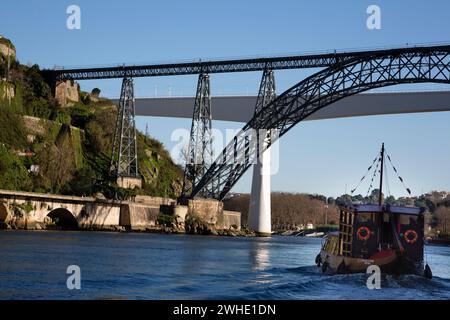 Una barca turistica naviga sotto il ponte Dona Maria Pia progettato da Gustav Eiffel e sullo sfondo il ponte Sao Joao a o Porto e sopra il Douro Foto Stock