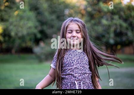 Hermosa muchacha rubia con gracia mientras disfruta de la naturaleza en un escenario al aire libre lleno de verdor y luz y recostada en el césped Foto Stock