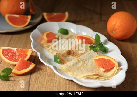 Suzette di crepes fatte in casa con foglia di arancia e menta su piatto ovale su tavolo di legno Foto Stock