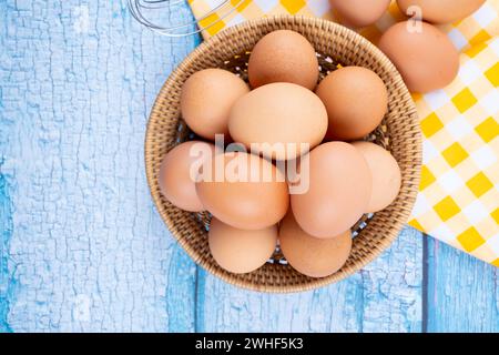 Vista dall'alto delle uova di gallina marroni nel cestino e una frusta su sfondo di legno blu. Foto Stock