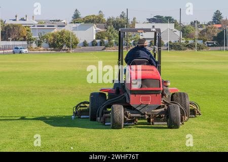 Vista posteriore di un giardiniere su un grande rasaerba per motociclisti che taglia un campo sportivo verde a Queenscliff, Victoria, Australia. Foto Stock