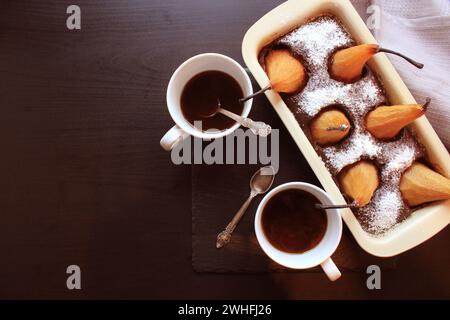 Pane al cioccolato torta con pere intere dentro al forno e due tazze di caffè su sfondo scuro. Vista superiore Foto Stock