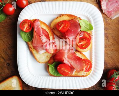 Bruschetta con prosciutto crudo, pomodorini e spinaci verde . Vista superiore Foto Stock