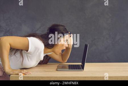 Giovane donna caucasica scioccata emotiva con volto sorpreso che guarda lo schermo di un notebook. Foto Stock