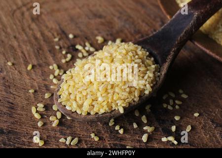 Grano bulgaro secco in cucchiaio di legno isolato bulgur versato Foto Stock