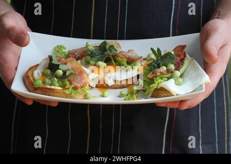 Bruschetta con rucola, chrispy bacon e uovo affogato servita su piastra bianca Foto Stock
