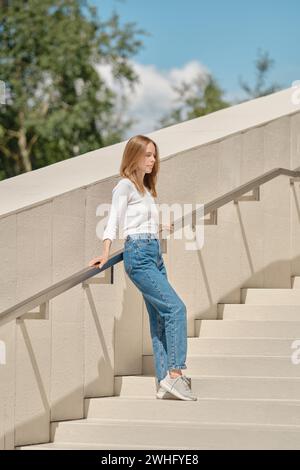 Donna in piedi con la schiena contro le ringhiere sulle scale che spargono le braccia Foto Stock