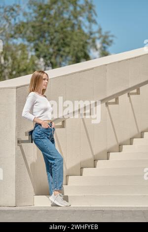 Donna in piedi sulle scale di profilo con le mani in tasca Foto Stock