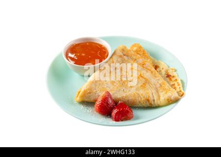 Crepes fatte in casa piegate in triangoli con marmellata di pesca e fragole su piatto blu isolato su sfondo bianco Foto Stock