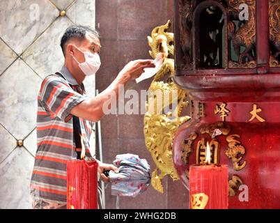 Un uomo brucia carta joss in un tempio di Bangkok. Le carte Joss sono carte fatte con modelli, colori e simboli specifici per imitare oggetti di valore come denaro, oro, case e auto. Si ritiene che l'atto di bruciarli crei un legame con l'aldilà, inviando le offerte ai membri della famiglia deceduti. La gente crede che la persona deceduta avrà una vita migliore attraverso questo rituale. Capodanno cinese 2024 a Chinatown, Bangkok, Thailandia, Sud-Est asiatico, sabato, 10 febbraio 2024, a partire da un anno del drago di legno. Foto Stock