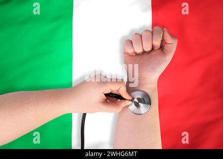 La testa di uno stetoscopio medico sul polso (primo piano) sullo sfondo della bandiera italiana. Concetto di sistema sanitario italiano Foto Stock