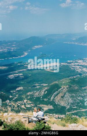 La sposa e lo sposo sono seduti su una panchina su una montagna sopra la Baia di Cattaro Foto Stock