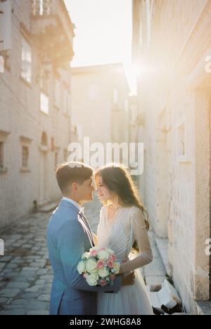 Lo sposo bacia quasi la sposa con un bouquet su una stradina stretta di una città vecchia Foto Stock