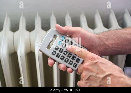 Le mani di un uomo con una calcolatrice calcolano i costi energetici di un sistema di riscaldamento inefficiente, concetto di finanziamento domestico, gonfiat Foto Stock