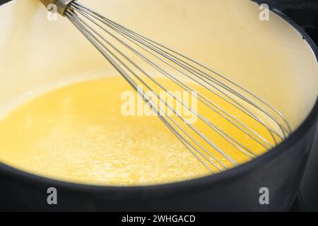 Frusta con filo metallico in una pentola con salsa di semola gialla dorata o budino, cuocere un delizioso dessert, copiare spazio, focalizzazione selezionata Foto Stock