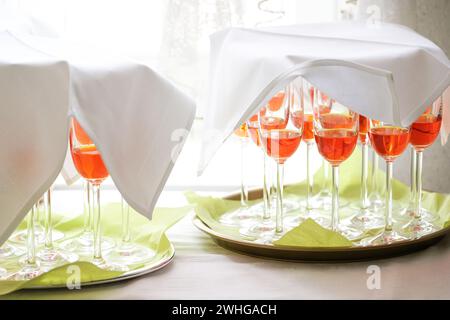 Cocktail Orange aperol in bicchieri da champagne ricoperti di tovaglioli bianchi su vassoi verdi, preparati come aperitivo per un evento festivo Foto Stock