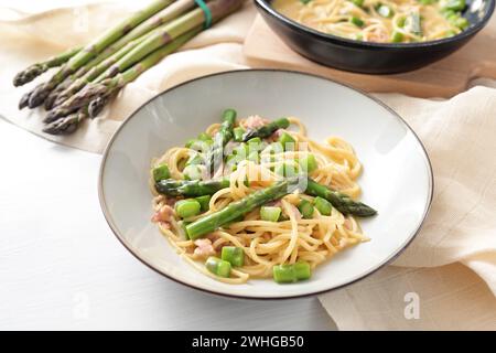 Spaghetti alla carbonara con asparagi verdi serviti in un piatto, ingredienti e tovagliolo su un tavolo bianco, spazio copia, selez Foto Stock