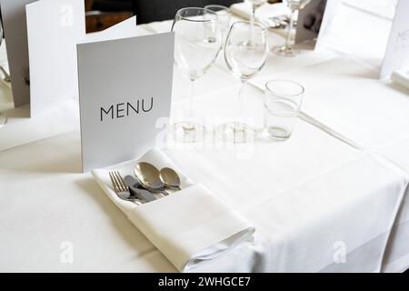 Ambiente elegante con menu a carte, vari bicchieri, posate e tovagliolo su un tavolo con tovaglia bianca per una cena di gala, Foto Stock