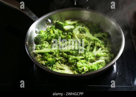 Broccoli tagliati a fette in una padella in acciaio inox su una stufa nera, cottura sana con verdure fresche, concentrazione selezionata Foto Stock