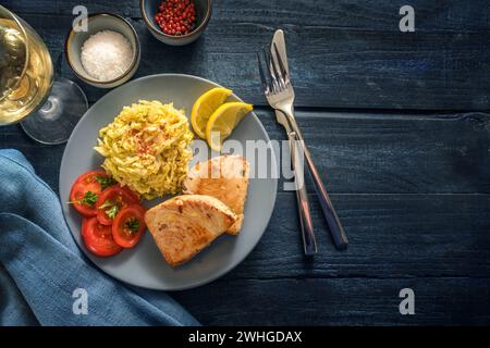 Gustosa portata di pesce con bistecche di tonno fritte, cavolo savoy, pomodori e limone serviti con vino, spezie e posate su ru blu scuro Foto Stock