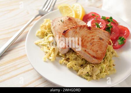 Due bistecche di tonno al cavolo savoy con pomodori e fette di limone su un piatto bianco e un tavolo di legno chiaro, spazio per copiare Foto Stock