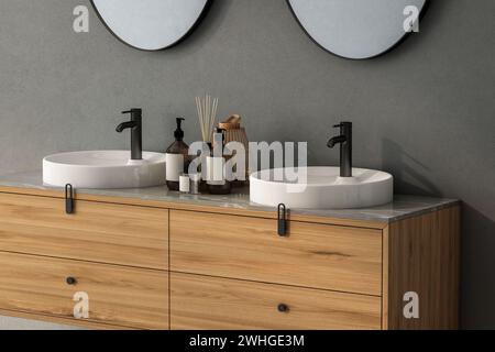 Primo piano di un doppio lavandino con specchi ovali - appeso su una parete grigio scuro, armadietto moderno con rubinetti neri nel bagno minimalista Foto Stock
