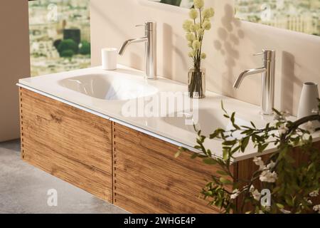 Primo piano di doppio lavabo con specchi in piedi su una parete beige, armadietto in legno con rubinetti nella stanza da bagno minimalista. Foto Stock