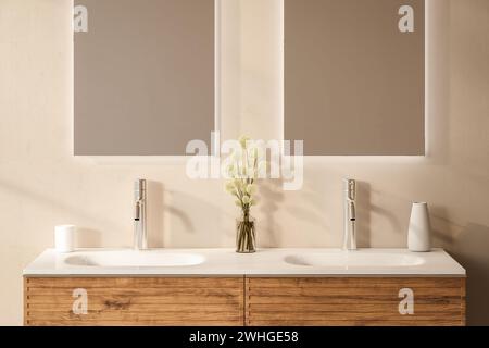 Primo piano di doppio lavabo con specchi in piedi su una parete beige, armadietto in legno con rubinetti nella stanza da bagno minimalista. Foto Stock