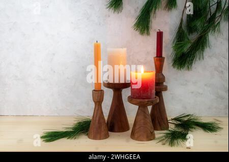 Quattro candele su piedistalli in legno, una è accesa per il primo Avvento, decorazione del ramo di pino, tavola di legno chiaro e stucco rustico ba Foto Stock