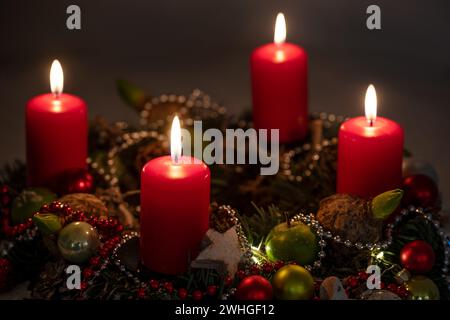 Luci dell'avvento e di Natale, quattro candele rosse su una corona con decorazioni su sfondo scuro, spazio copia, messa a fuoco selezionata Foto Stock