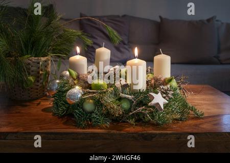 Secondo Avvento, corona con due candele bianche bruciate e decorazioni natalizie su un tavolo di legno di fronte al divano, festa Foto Stock
