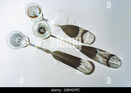 Tre diversi bicchieri da bere pieni d'acqua gettano lunghe ombre su sfondo grigio e piccole pozzanghere in cui il Foto Stock