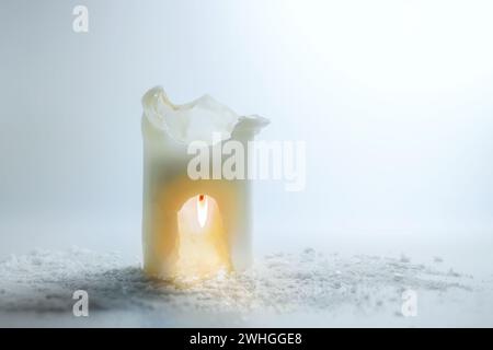 La candela bianca sta bruciando capovolta in una scultura, risparmiando calore ed energia, surreale natura morta delle vacanze invernali, ba grigio chiaro Foto Stock