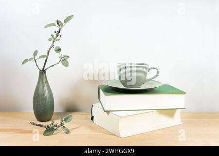 Scrivania o tavolo in legno con libri, una tazza da tè verde e ramoscelli di salvia in un piccolo vaso di ceramica su una parete bianca grigia, spazio per copiare, s Foto Stock